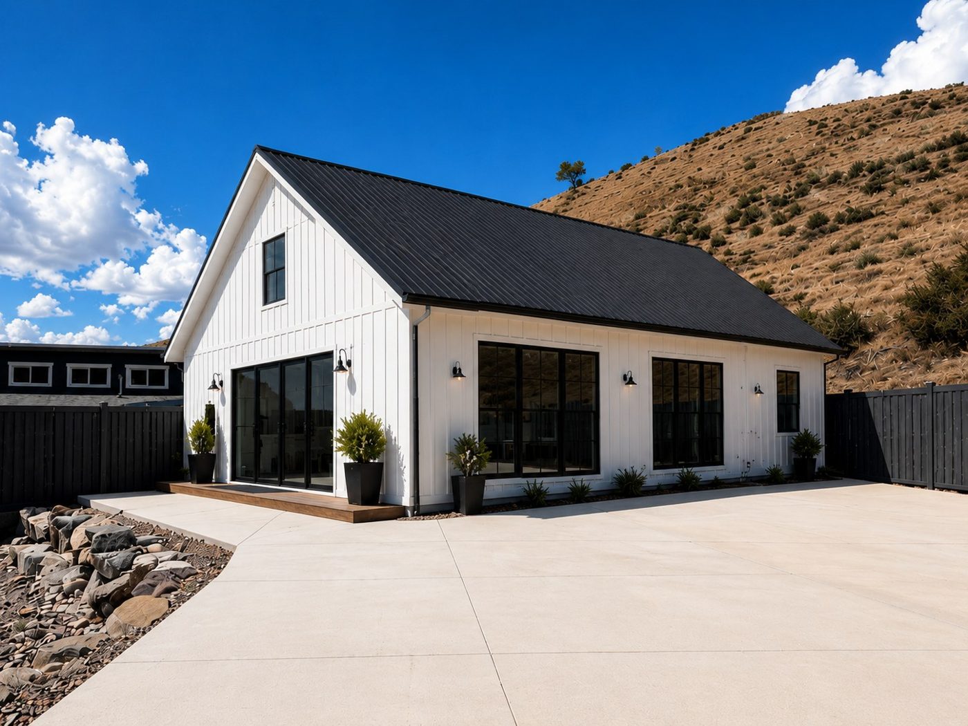 A white board-and-batten Cocoon ADU with a black metal roof and large black-framed windows on a hillside lot